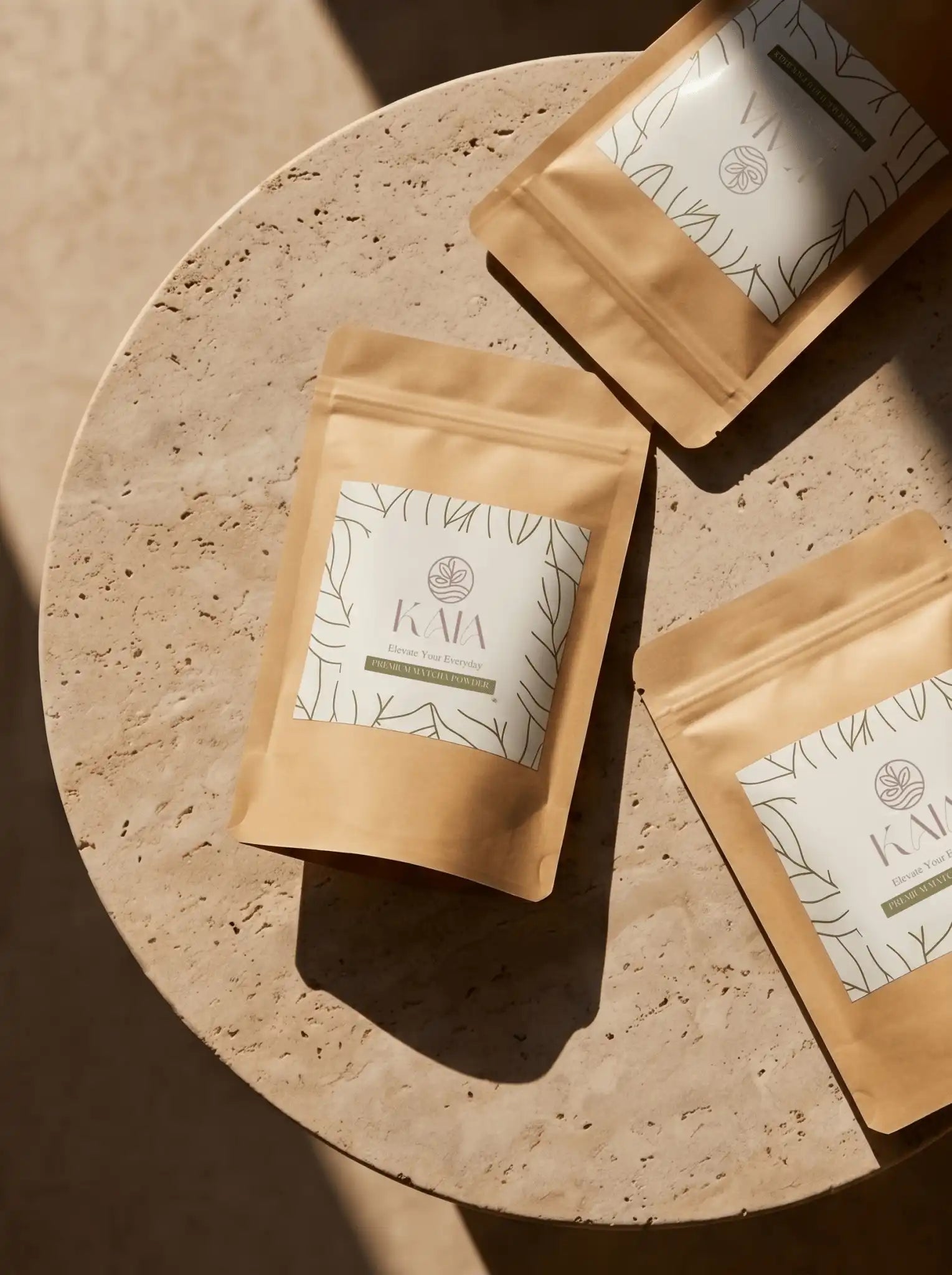 Top-down view of three KAIA Origin premium matcha powder pouches on travertine, flat lay editorial of Belgian stone-ground matcha